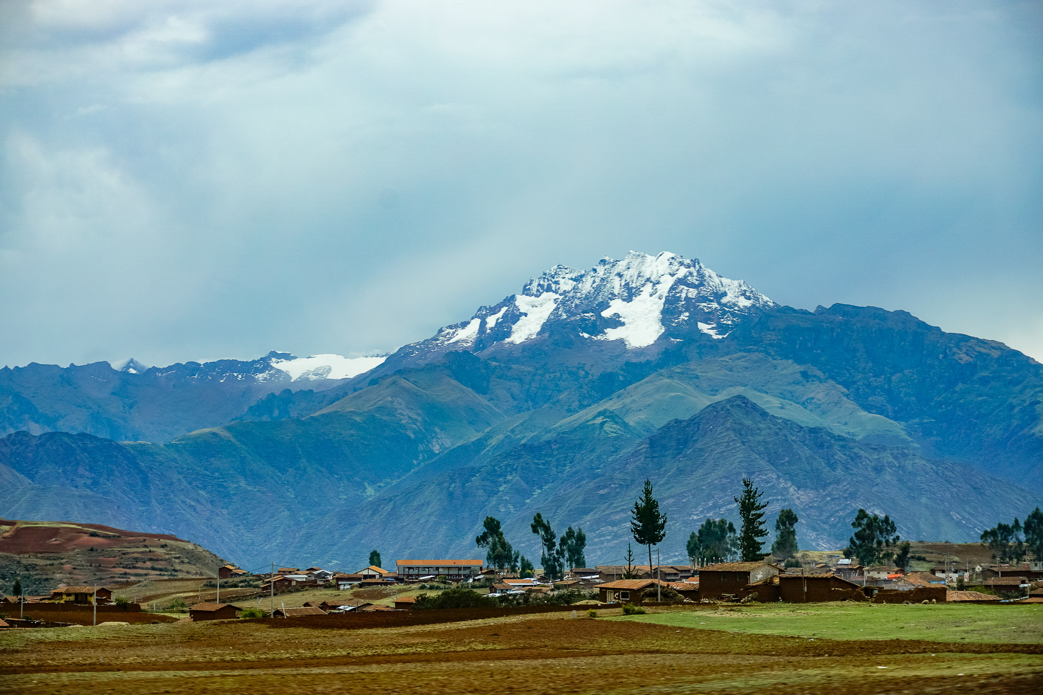 A picturesque village nestled in the foreground of a majestic Peruvian Andes mountain range, showcasing nature's beauty.